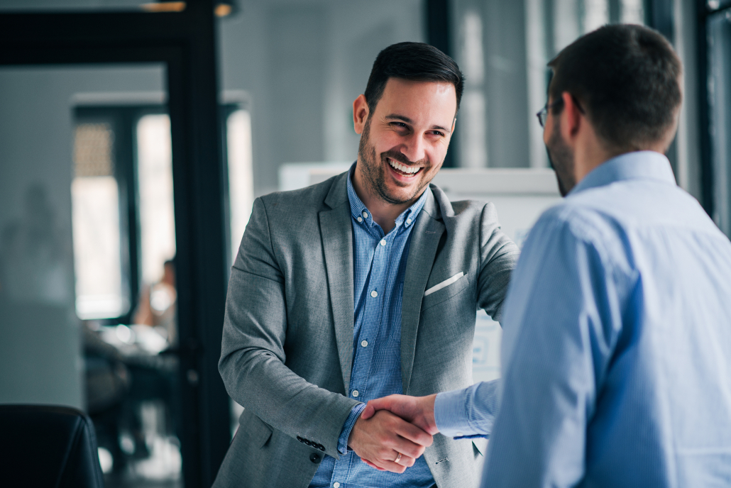 Portrait of cheerful young manager handshake with new employee. Zwei Geschäftsmänner schütteln sich lächelnd die Hand in einem modernen Büro